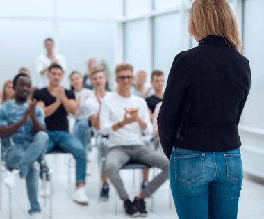 Konferans odasında seyircilerin önünde duran genç bir kadın.