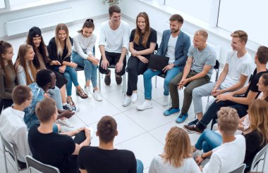 Geniş bir grup genç insan bir çemberin içinde oturuyor.