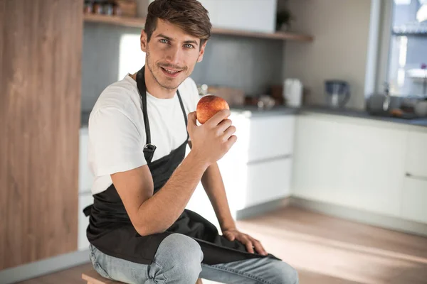 Vonzó férfi egy almát ül egy otthoni konyhában — Stock Fotó