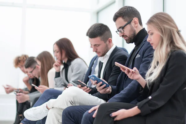 Groupe de jeunes gens d'affaires avec smartphones assis dans une rangée . — Photo