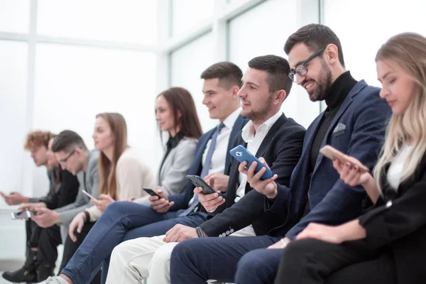 Groupe de jeunes gens d'affaires avec smartphones assis dans une rangée . — Photo