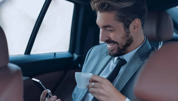 Empresario bebiendo café en coche con teléfono en la mano — Foto de Stock