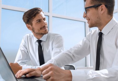 Genç ofis çalışanı gülümsüyor, iş arkadaşları arka grupta çalışıyor.