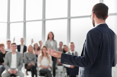 Kapat. Konuşmacı konferans odasında seyircilerin önünde duruyor.