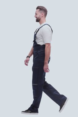 Yan görünüş. Tulum giymiş gülümseyen adam özgüvenle ileriye doğru ilerliyor.
