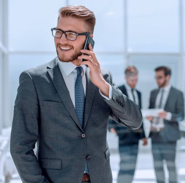Banka ofisinin yanında cep telefonu olan bir işadamı duruyor.