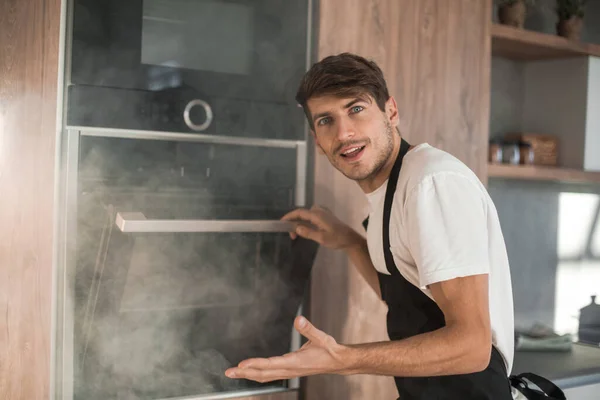 Frustrated young man standing near broken oven — Stock Photo, Image
