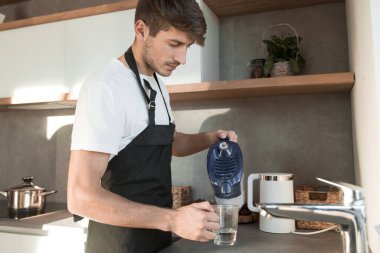 Genç adam bardağa temiz su dolduruyor.