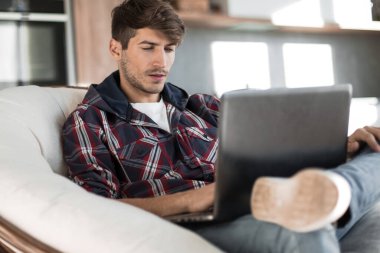 Kapat. Dizüstü bilgisayarı olan çekici bir adam sandalyede oturuyor.