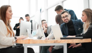 Genç girişimci ve çalışma grubu ofis masasında oturuyor.