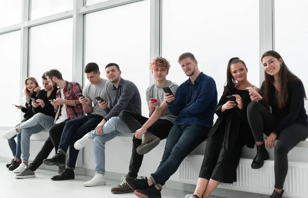 Ofis penceresinin yanında oturan akıllı telefonları olan gülümseyen genç insanlar.. — Stok fotoğraf