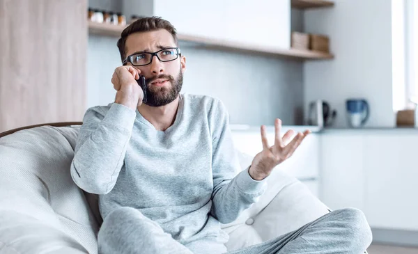 Hombre alegre hablando en un teléfono móvil sentado en una silla cómoda — Foto de Stock