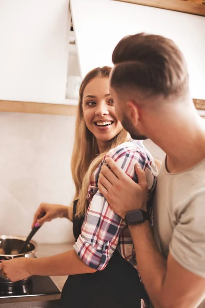 Egy fiatalember viccelődik a feleségével a konyhában. — Stock Fotó