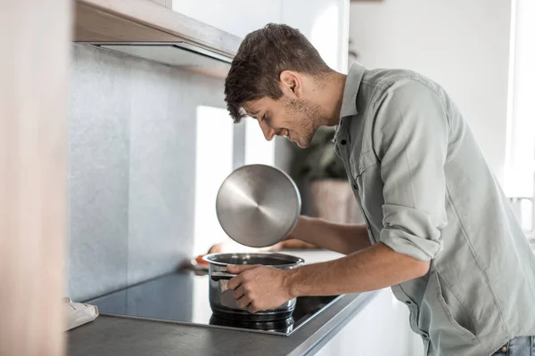 Glad ung man tittar in i en kruka med läcker mat. — Stockfoto