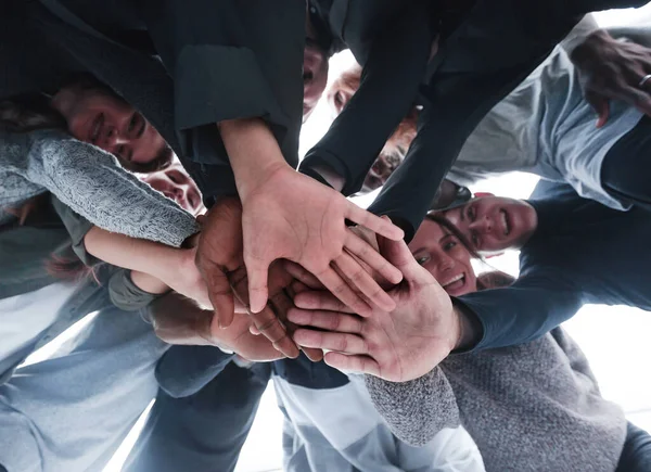 Vue du bas. groupe de jeunes gens heureux faisant une tour de leurs mains . — Photo