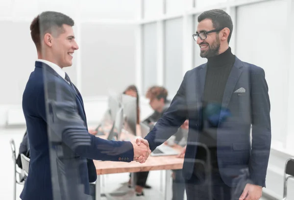 Através do vidro. handshake parceiros de negócios no escritório — Fotografia de Stock