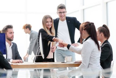 Ofis masasının yanında el sıkışan iki genç kadın..