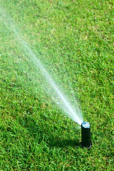 Aspersor rociando agua sobre un césped verde —  Fotos de Stock