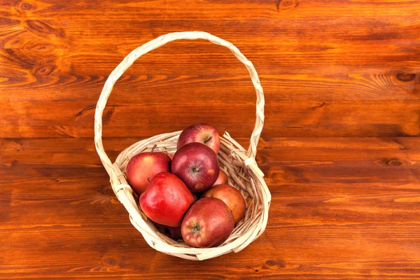 Rijpe rode appels in rieten mand op houten tafel . — Stockfoto