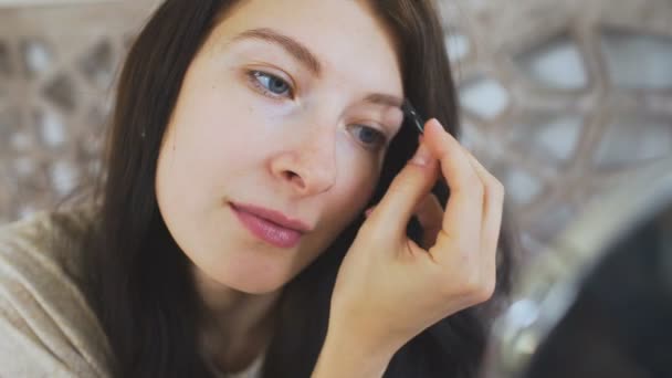 Hermosa mujer sosteniendo un espejo y dibujando cejas en la cara - inventar conceptos — Vídeo de stock