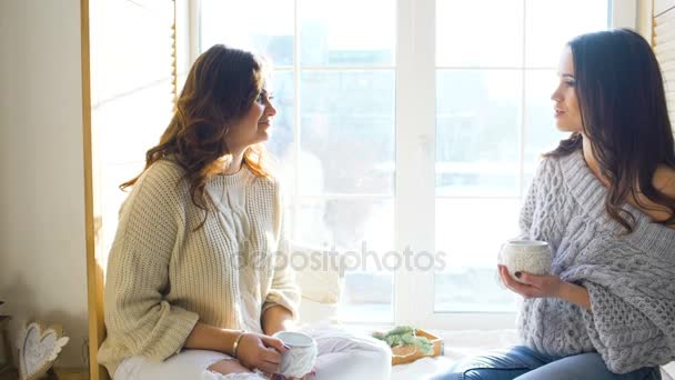 Dos hermosas chicas sonriendo mientras están sentadas en la ventana. Novias divirtiéndose y riendo en el dormitorio . — Vídeos de Stock