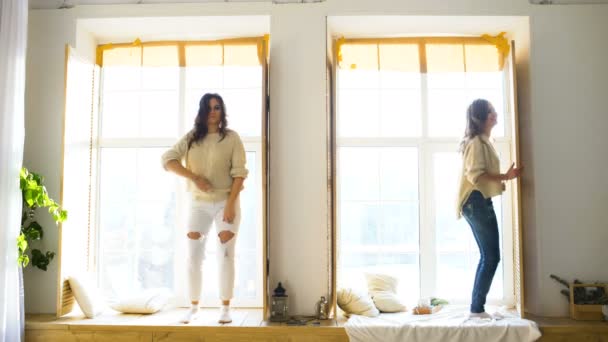 Счастливые и красивые подруги танцуют у окна, веселясь и радуясь в спальне — стоковое видео