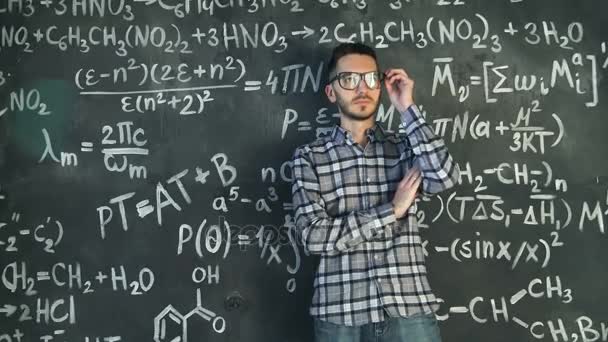 Joven científico hombre limpiar sus gafas en química y matemática ecuaciones pared habitación interior — Vídeos de Stock