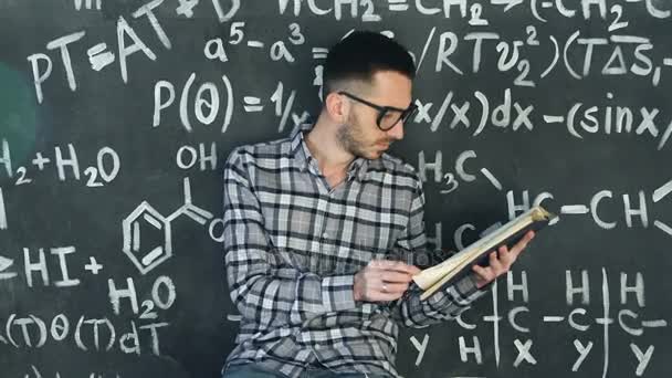 Mladý vědec člověk přečíst knihu v chemických a matematických rovnic nástěnné vnitřní — Stock video