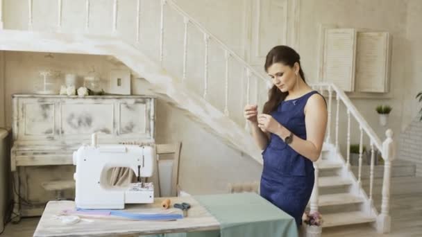 Junge Bekleidungsdesignerin und Näherin nähen mit Faden und Nadel in der Nähe der Nähmaschine — Stockvideo