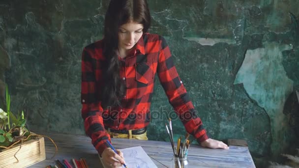 Молодая художница рисует портрет на бумажном блокноте, глядя в камеру — стоковое видео