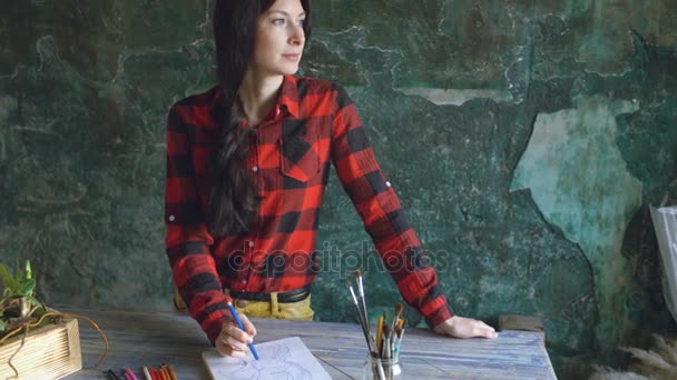 Young woman artist painting scetch on paper notebook with pencil looks in window — Stock Video