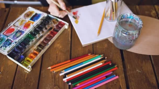 Joven artista dibujar pictrure con acuarela pinturas y pincel mezclando colores de primer plano — Vídeos de Stock