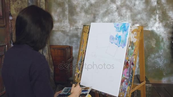 Joven artista dibujar pictrure con pinturas de acuarela y pincel sobre lienzo de caballete — Vídeos de Stock