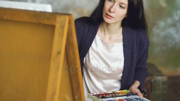Jonge vrouw kunstenaar trekken pictrure met aquarel verf en penseel op ezel doek — Stockvideo