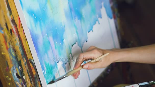 Νεαρή γυναίκα καλλιτέχνης επιστήσω ανέκδοτα με τα χρώματα watercolor και βούρτσα στο καβαλέτο καμβά closeup χέρι — Αρχείο Βίντεο