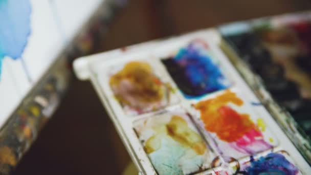 Νεαρή γυναίκα καλλιτέχνης επιστήσω ανέκδοτα με τα χρώματα watercolor και βούρτσα στο καβαλέτο καμβά closeup χέρι — Αρχείο Βίντεο