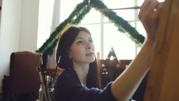 Молода жінка-художниця малює малювання акварельними фарбами та пензлем на мольберті — стокове відео