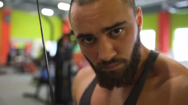 Bonito homem desportivo está se exercitando olhando para a câmera no clube de fitness — Vídeo de Stock