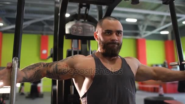 Hombre deportivo guapo está haciendo ejercicio mirando a la cámara en el club de fitness — Vídeos de Stock