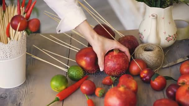 Жінка-кухар бере гранат з дерев'яного столу з фруктами та овочами, готуючи перед приготуванням — стокове відео