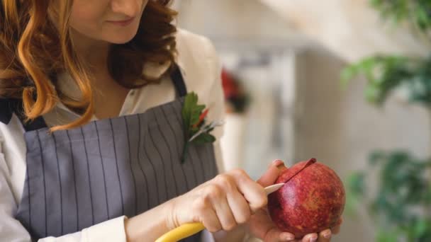 Chef donna cuoco in grembiule tagliato melograno con coltello primo piano in cucina — Video Stock