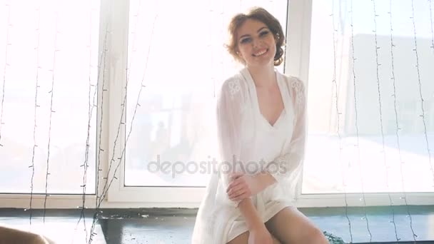 Portrét krásné mladé nevěsty pózování a úsměv do kamery žena sedí na okně v ložnici — Stock video