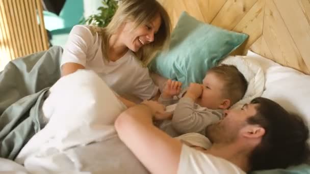 Счастливая семья просыпается и играет в постель дома — стоковое видео
