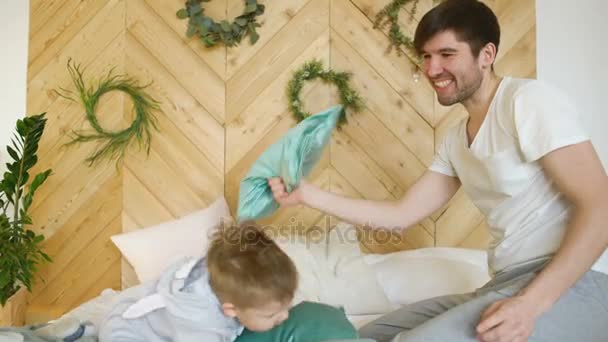 Positive father and son having fun and fight piloows on bed at home — Stock Video