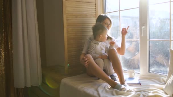 Matka z dzieckiem siedzi w oknie i grać — Wideo stockowe