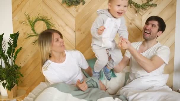 Uma jovem família com filho brincando na cama no quarto — Vídeo de Stock