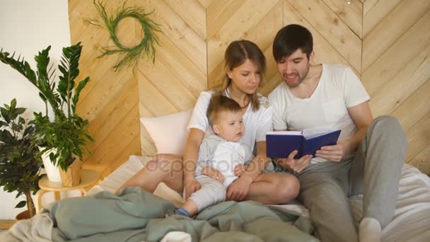 Família amorosa de três deitado na cama de manhã. Abraço familiar e livro de leitura — Vídeo de Stock