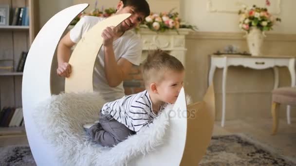 快乐的父亲坐在地板上玩儿子坐在椅子上 — 图库视频影像