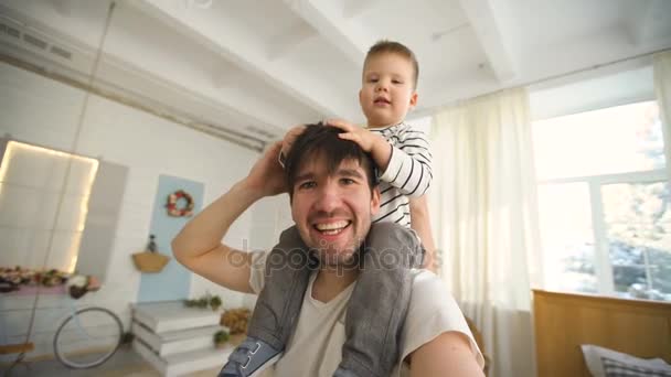 Feliz padre llevando a su hijo sonriente en el cuello y haciendo selfie en video en el dormitorio — Vídeo de stock