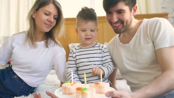 Famille souriante célébrant leur anniversaire de fils ensemble avant de souffler des bougies sur le gâteau — Video